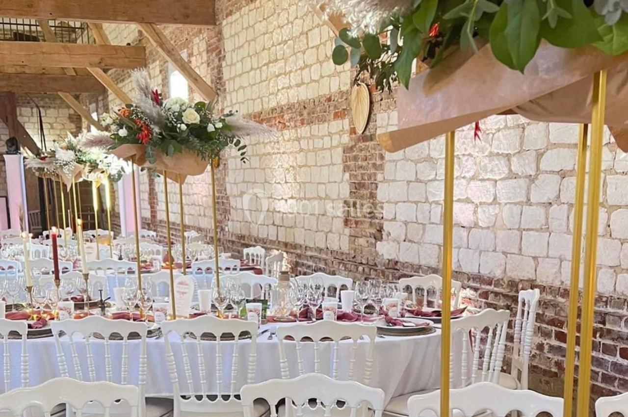 Salle de réception décorée avec des tables dressées, des chandeliers, et des compositions florales suspendues.