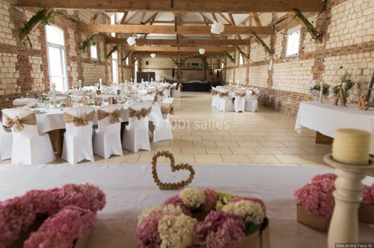 Salle de réception décorée pour un mariage, avec tables dressées, chaises ornées de nœuds et fleurs en centre de table.