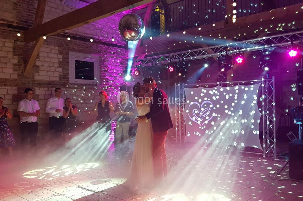 Un couple danse sous une boule à facettes dans une salle éclairée par des lumières colorées, entouré d'invités.