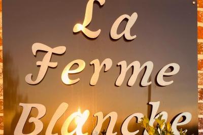 Panneau en métal avec l'inscription ’La Ferme Blanche’, reflétant la lumière du soleil couchant.