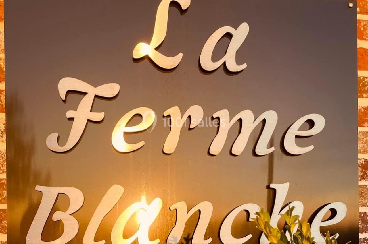 Panneau en métal avec l'inscription ’La Ferme Blanche’, reflétant la lumière du soleil couchant.