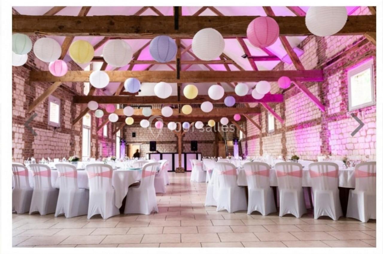 Salle de réception décorée avec des lanternes colorées suspendues, tables dressées et éclairage rose.