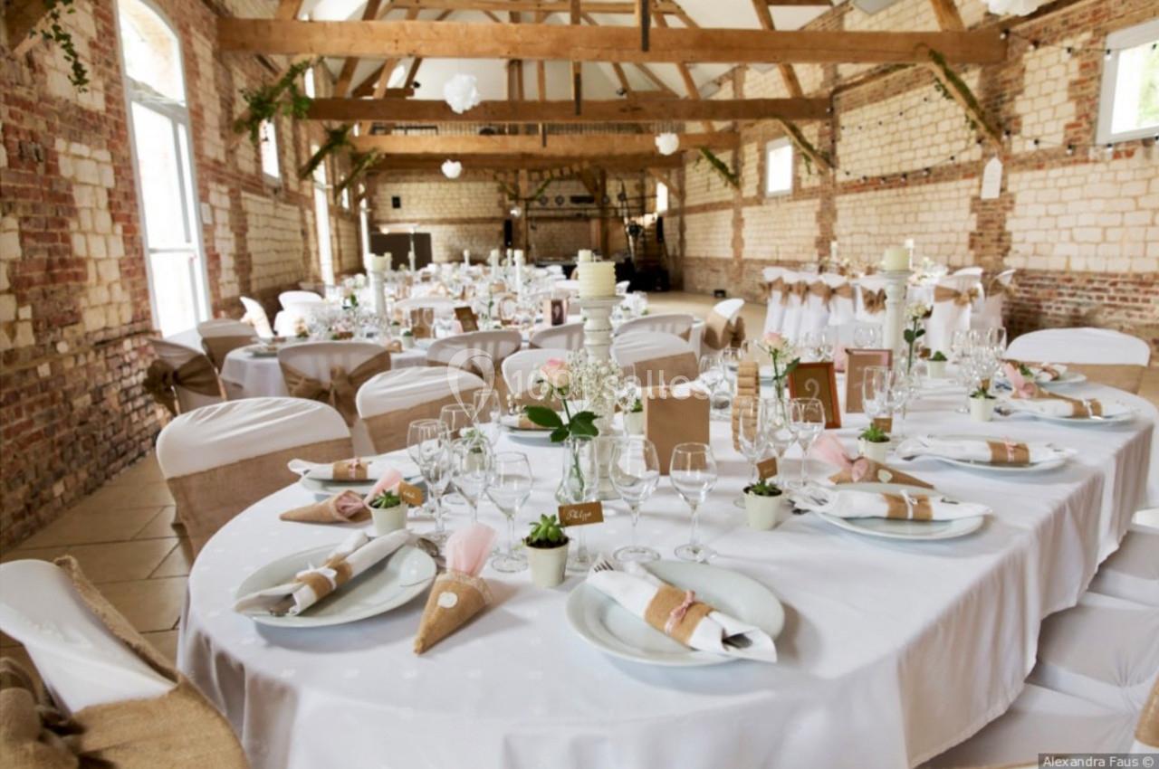 Salle de réception décorée pour un mariage, avec tables rondes dressées, nappes blanches et détails élégants.