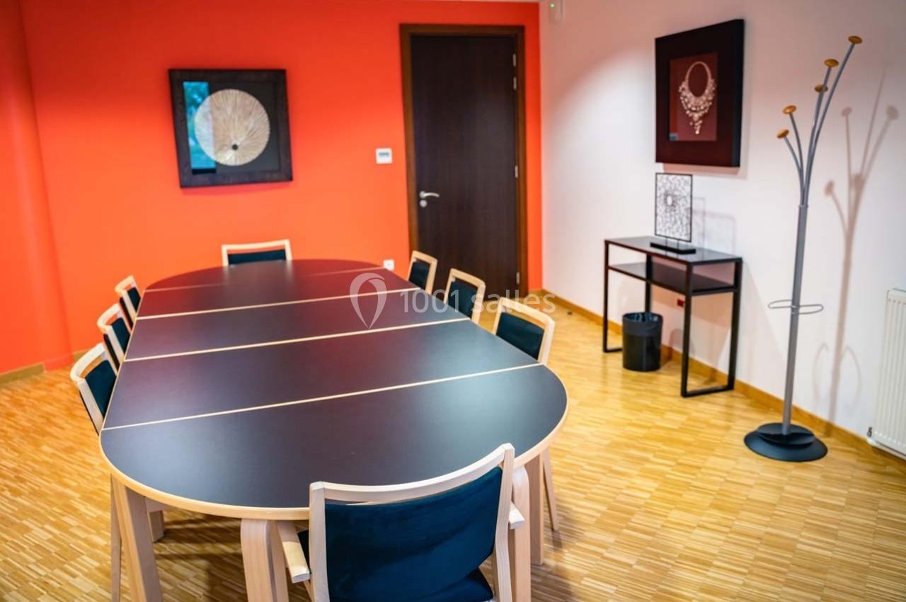 Salle de réunion avec une grande table noire, des chaises en bois, des décorations murales et un portemanteau.