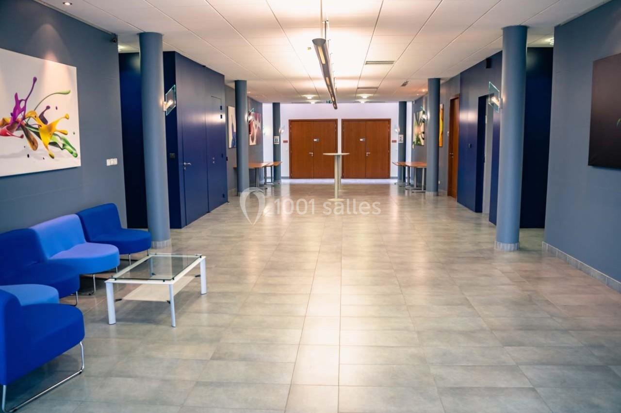 Un hall moderne avec des murs bleus, des fauteuils bleus, une table basse en verre et des œuvres d'art accrochées.