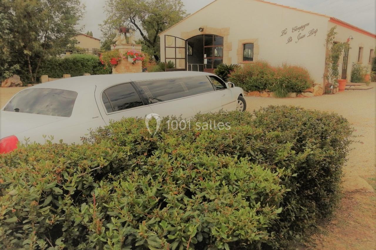 Une limousine blanche garée devant un bâtiment clair entouré de végétation et d'arbustes.