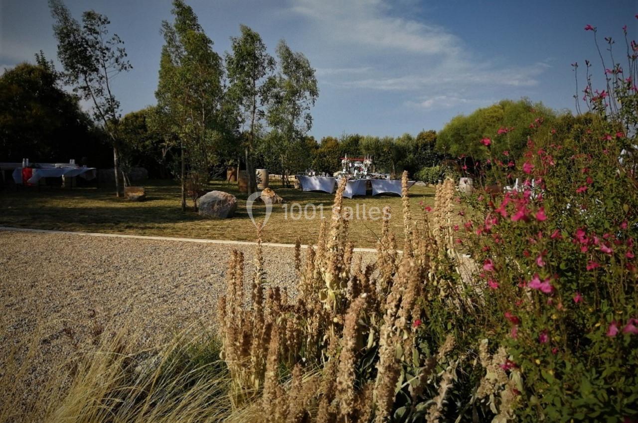 Jardin avec pelouse, allée gravillonnée, fleurs au premier plan et tables dressées en arrière-plan.