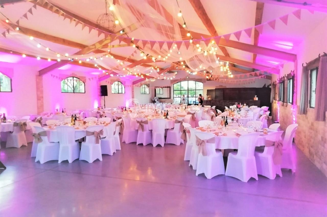 Salle de réception décorée avec des guirlandes lumineuses, des nappes blanches et des tables dressées pour un événement.