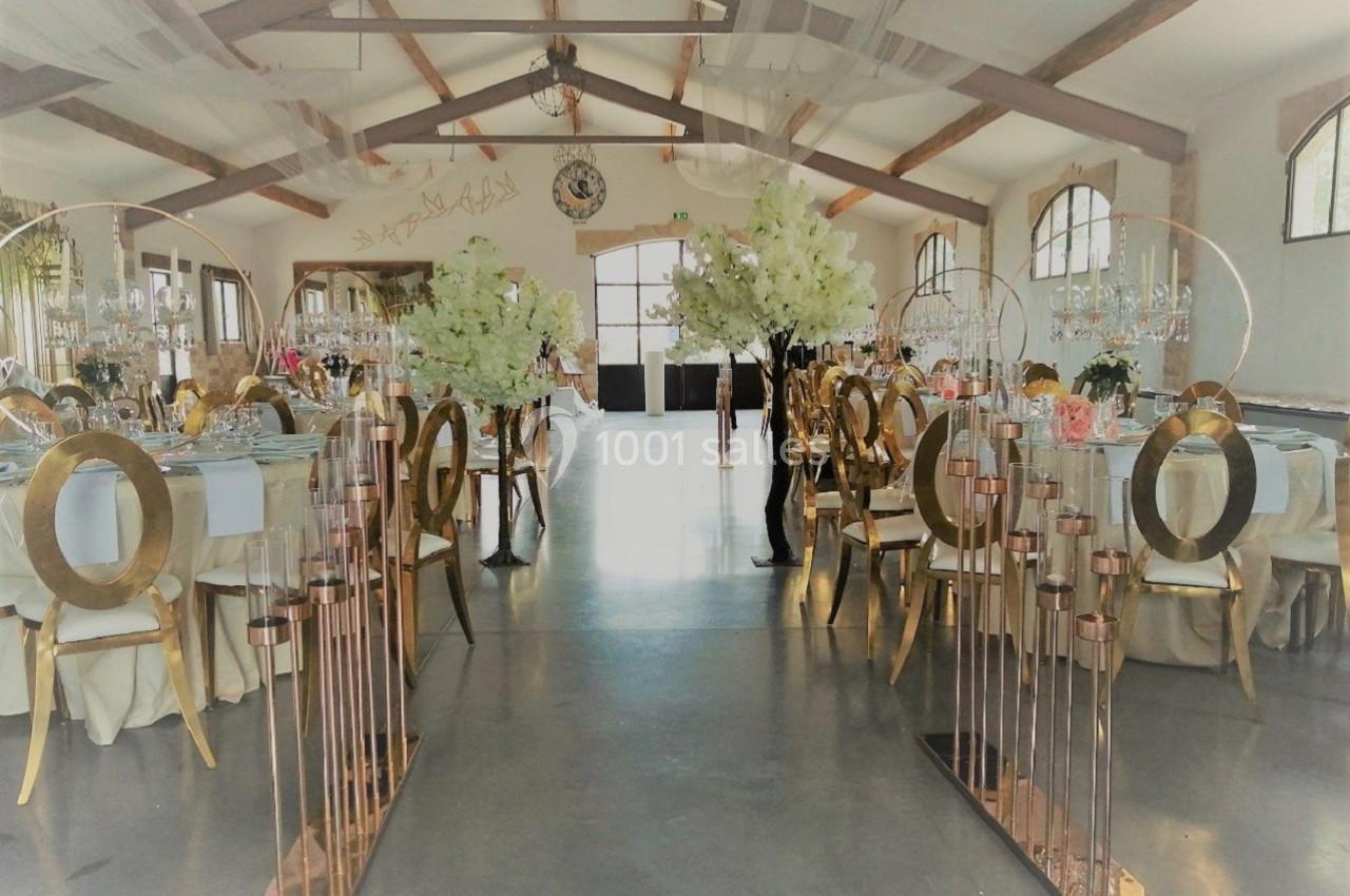 Salle de réception décorée avec des tables élégantes, des arches dorées et des compositions florales blanches.
