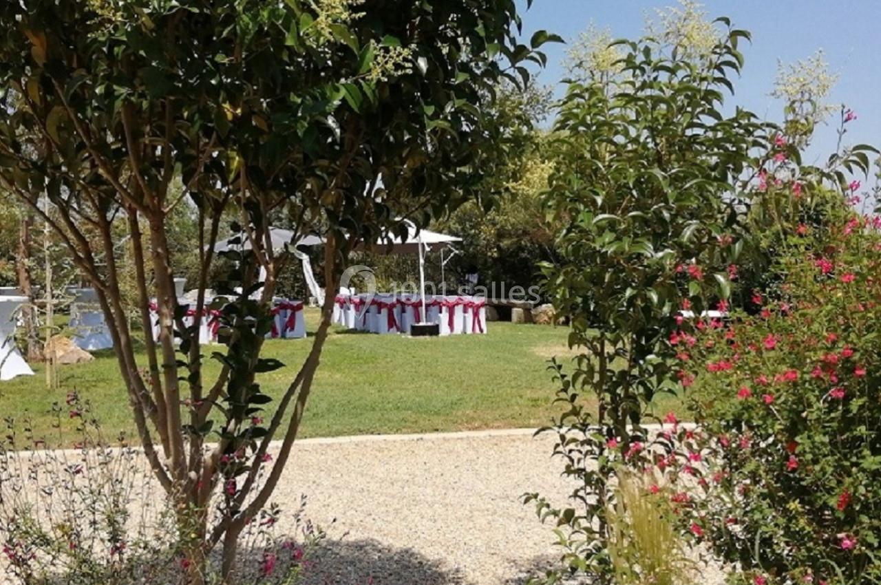 Jardin avec pelouse, arbres et tables décorées de nappes blanches et rubans rouges, sous un ciel dégagé.