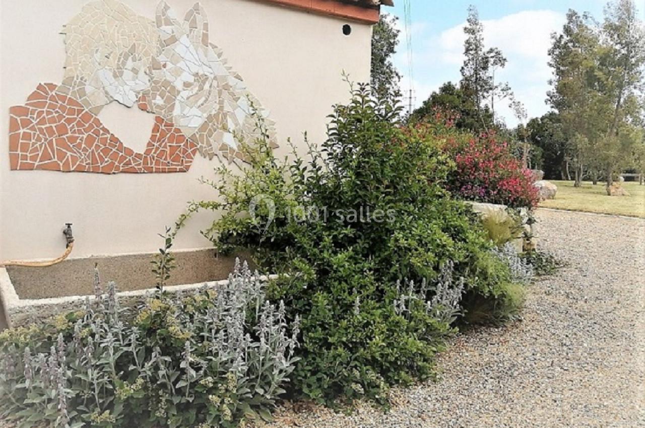 Fresque en mosaïque représentant un homme et un cheval sur un mur, entourée de plantes et d'un jardin.