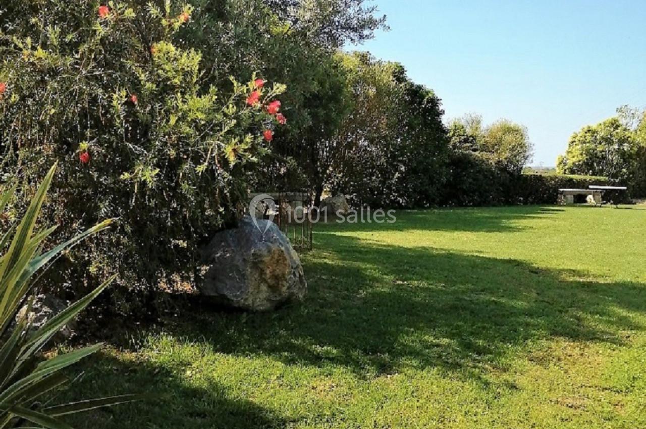 Espace vert avec pelouse, arbustes fleuris et arbres sous un ciel bleu clair.