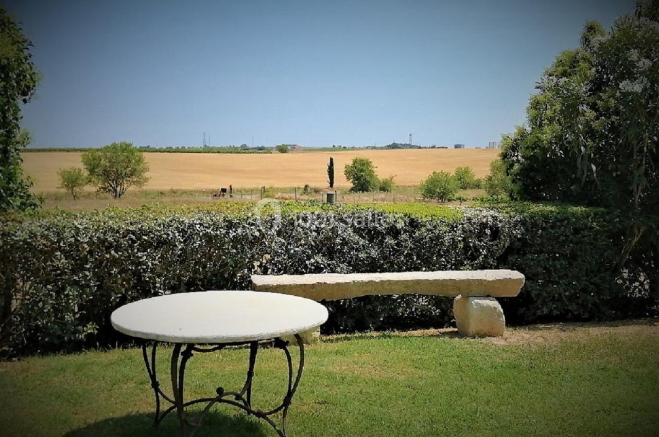 Table ronde et banc en pierre dans un jardin avec vue sur un champ doré et un ciel dégagé en arrière-plan.
