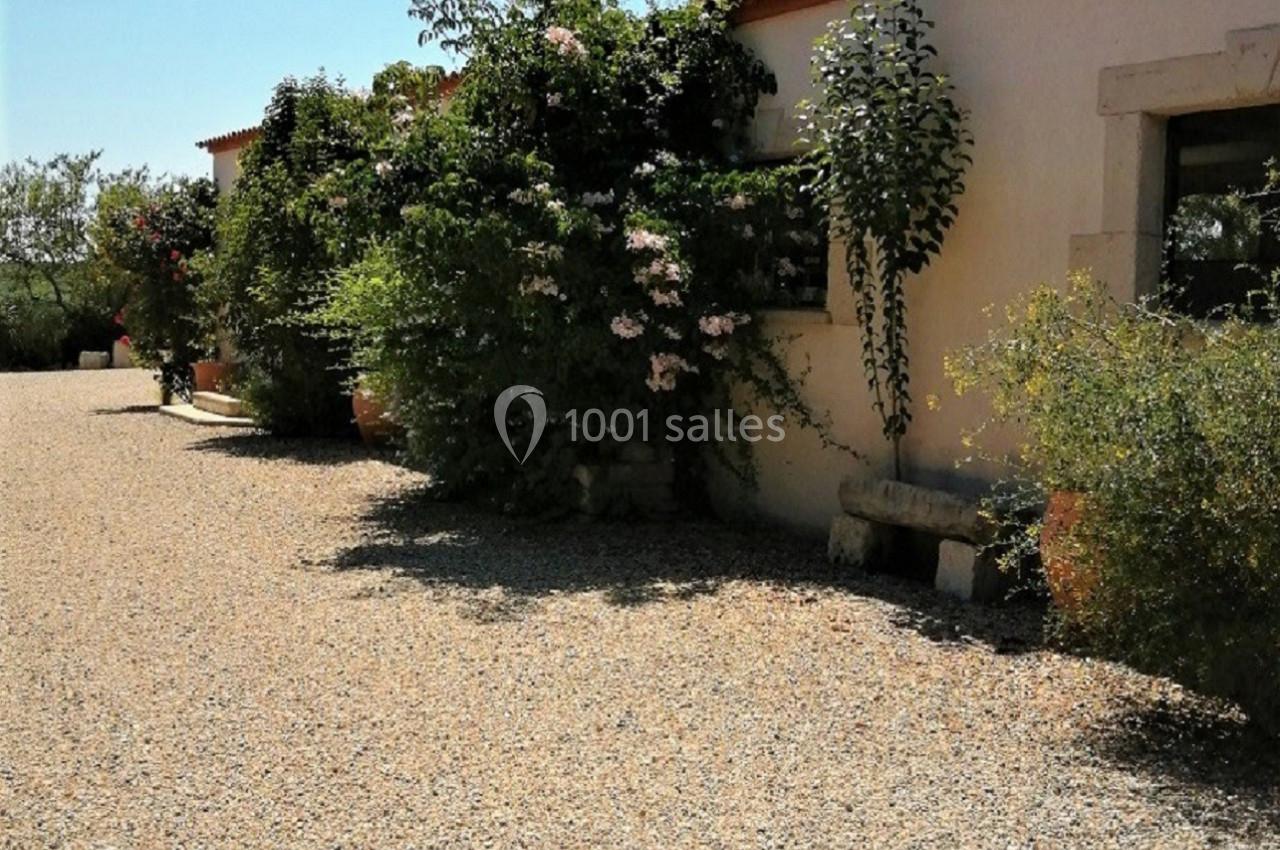 Façade d'une maison avec des murs clairs, des plantes grimpantes et une allée de gravier sous un ciel dégagé.