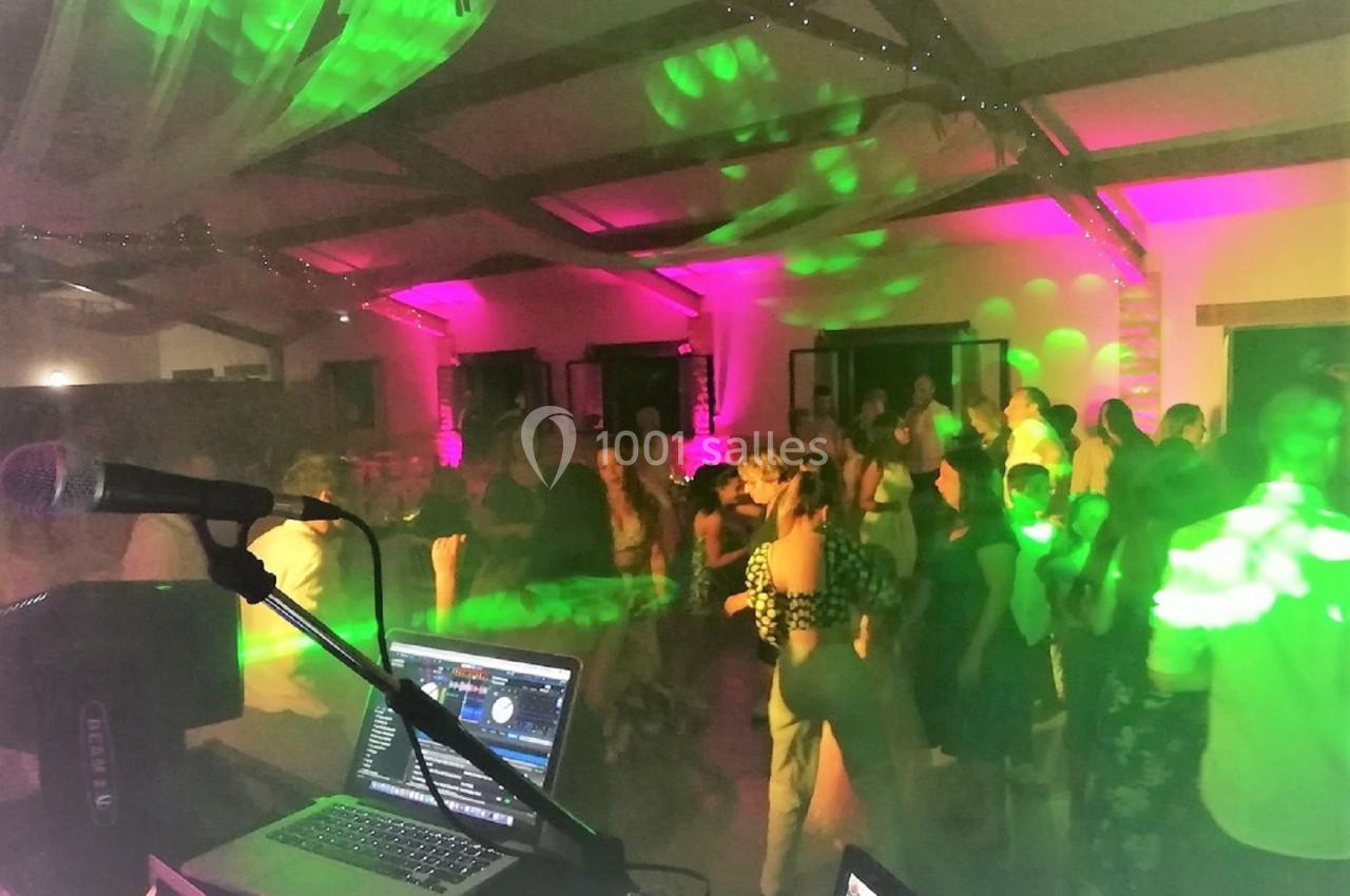 Groupe de personnes dansant dans une salle éclairée par des lumières colorées, vue depuis une table de DJ.