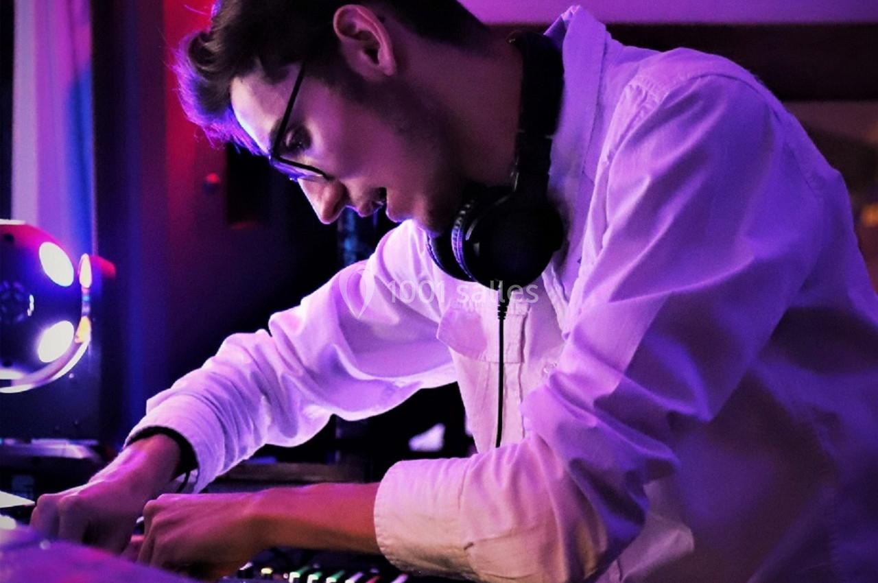 Un DJ en chemise blanche mixe de la musique sur une console dans une ambiance lumineuse violette.