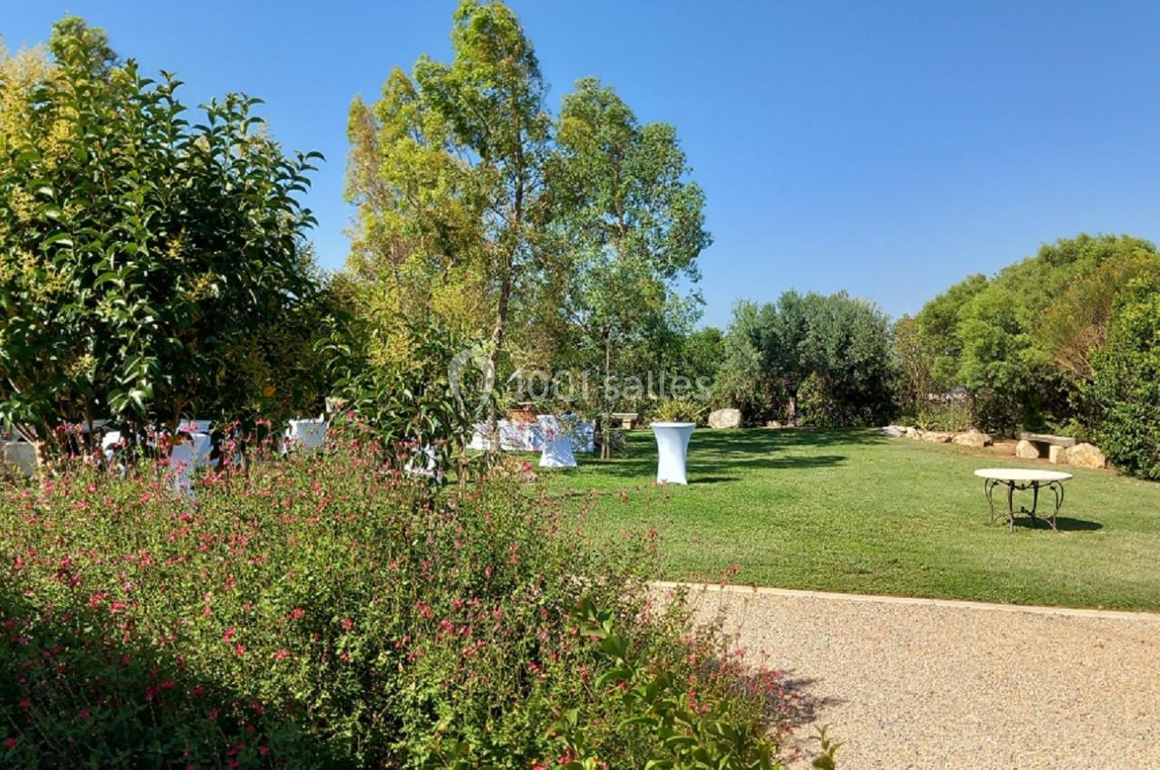 Jardin verdoyant avec pelouse, arbres, arbustes fleuris et tables installées pour un événement en plein air.