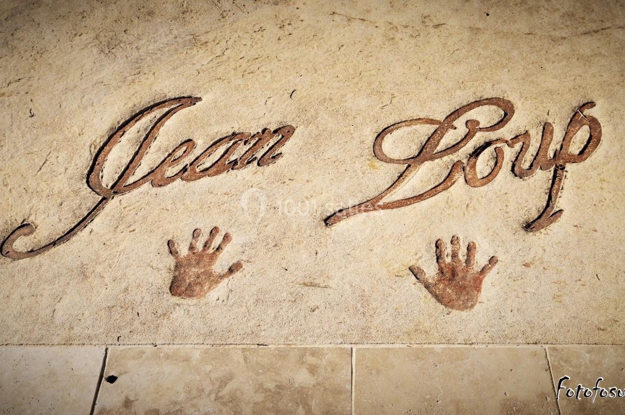 Inscription ’Jean Loup’ gravée dans une surface beige avec deux empreintes de mains en dessous.