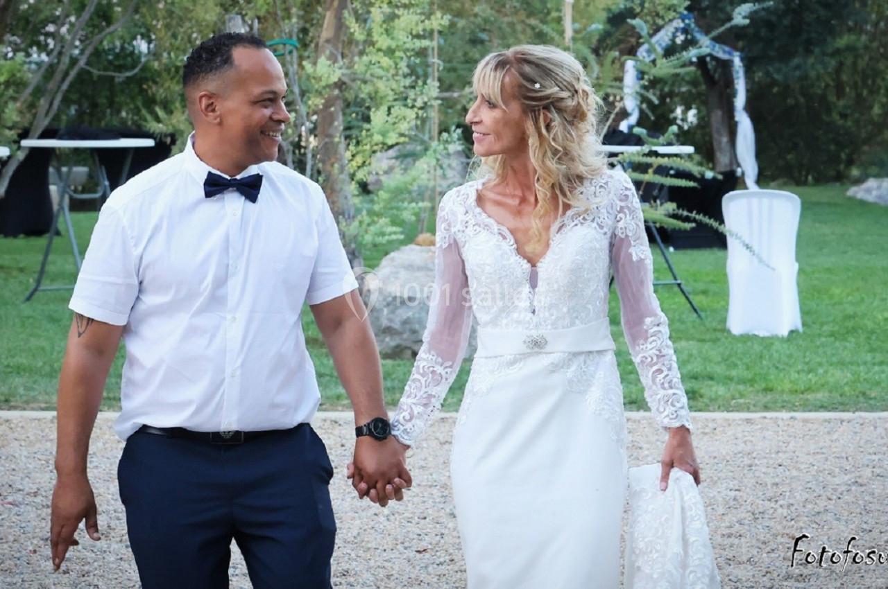 Un couple en tenue de mariage marche main dans la main dans un jardin.