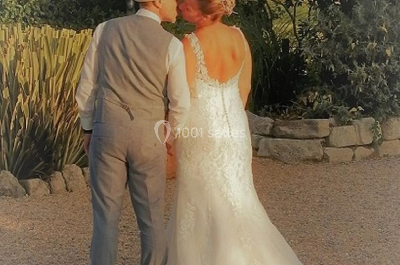 Un couple en tenue de mariage se tient la main et s'embrasse dans un jardin ensoleillé.