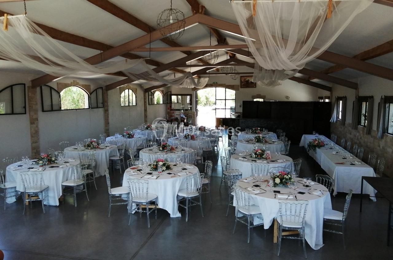 Salle de réception décorée avec des tables rondes dressées, nappes blanches et arrangements floraux.