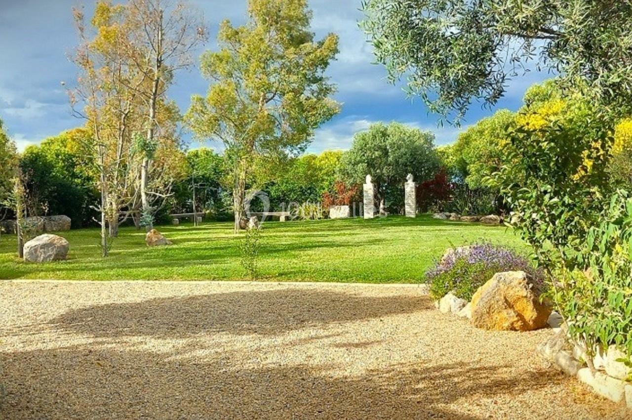 Jardin verdoyant avec pelouse, arbres, allée en gravier et quelques personnes près d'une table à l'arrière-plan.