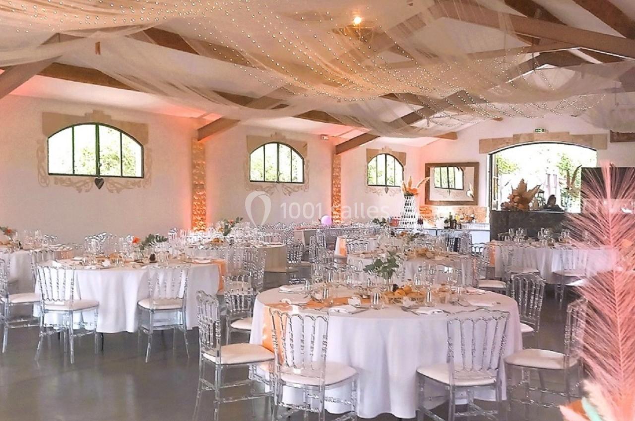 Salle de réception décorée avec des tables rondes, des chaises transparentes et un plafond orné de voilages lumineux.