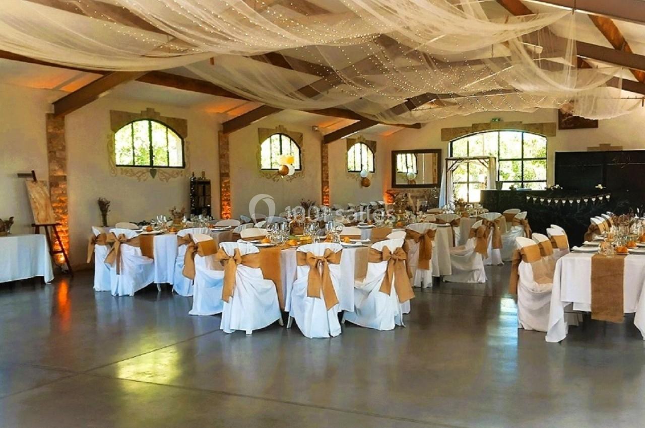 Salle de réception décorée pour un événement, avec tables rondes dressées et chaises ornées de nœuds beiges.