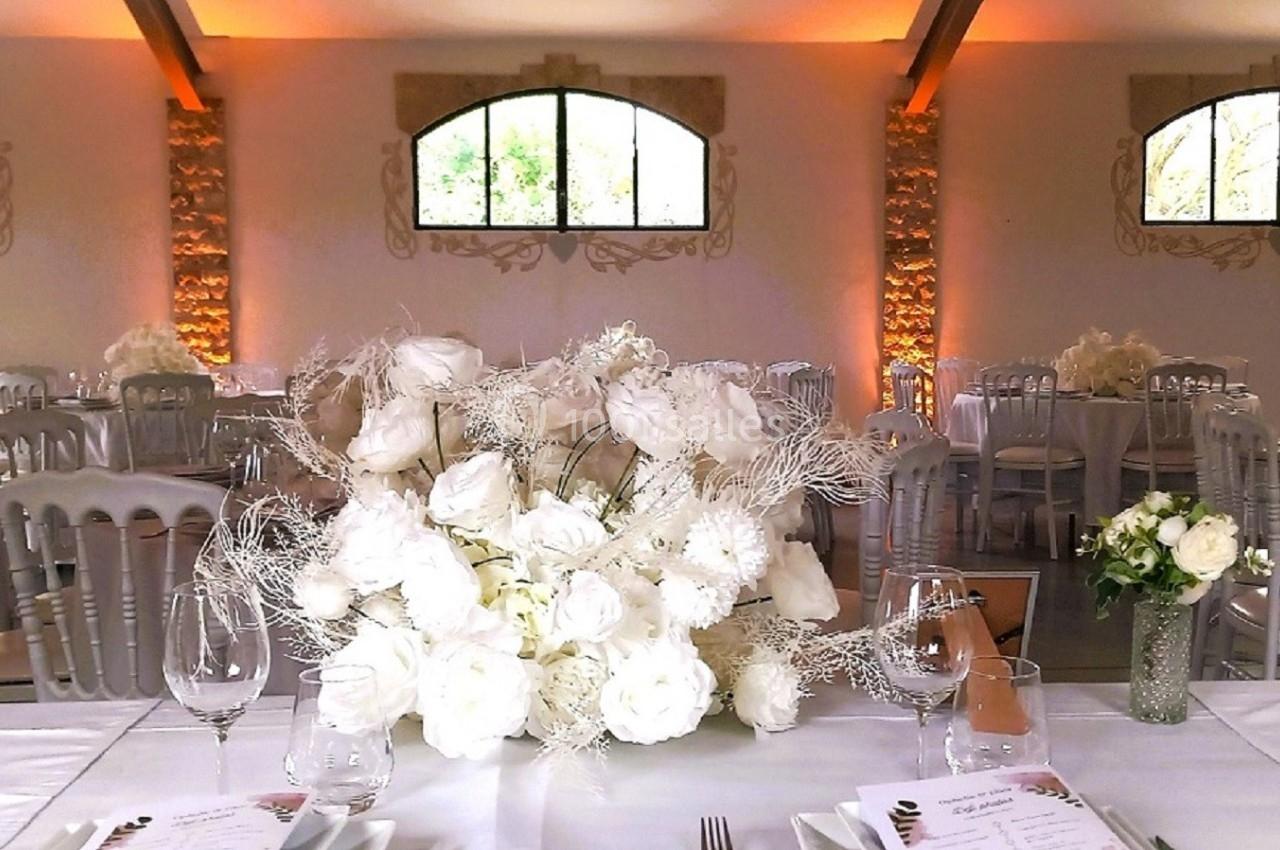 Salle de réception décorée avec des tables dressées, des bouquets de fleurs blanches et une lumière tamisée.