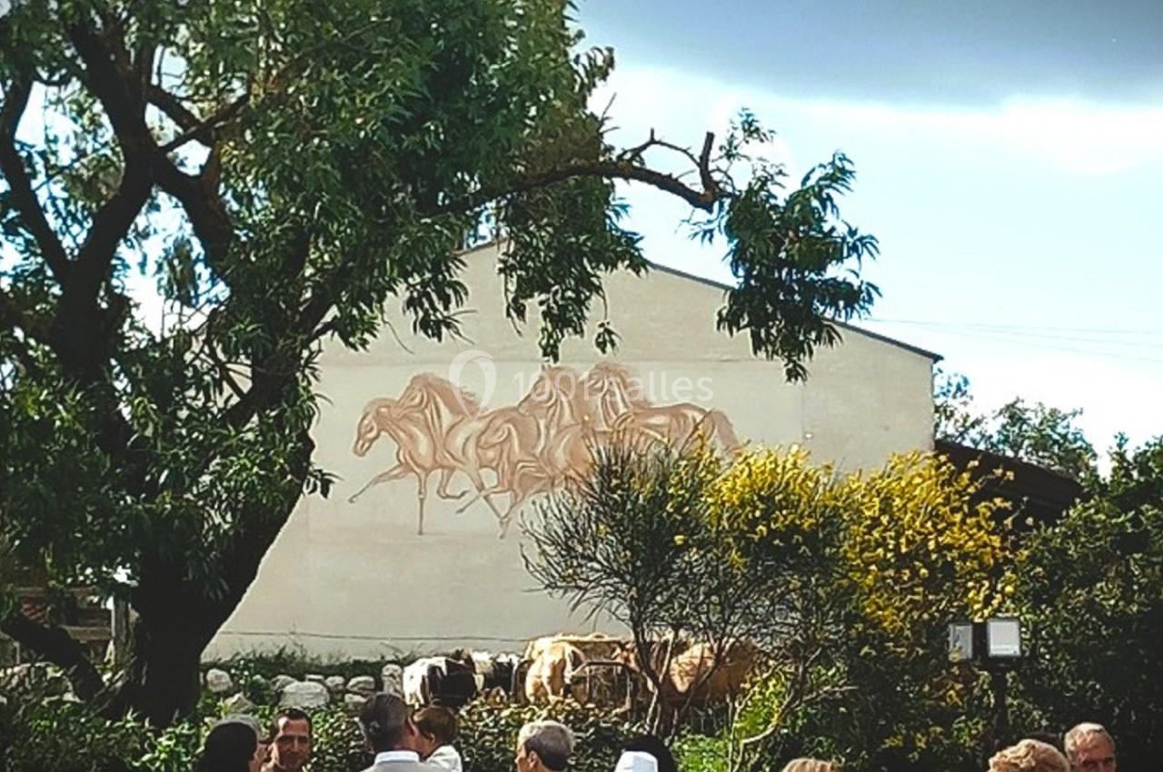 Fresque représentant des chevaux sur un mur blanc, entourée d'arbres et de végétation, avec des personnes au premier plan.