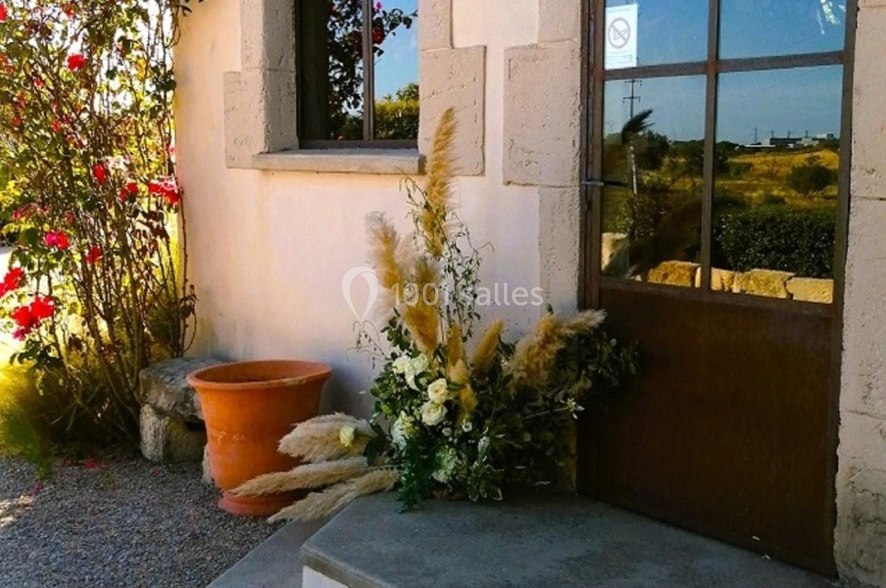 Entrée d'une maison en pierre avec porte vitrée, décorée de fleurs et de plantes, entourée de gravier et de rosiers.