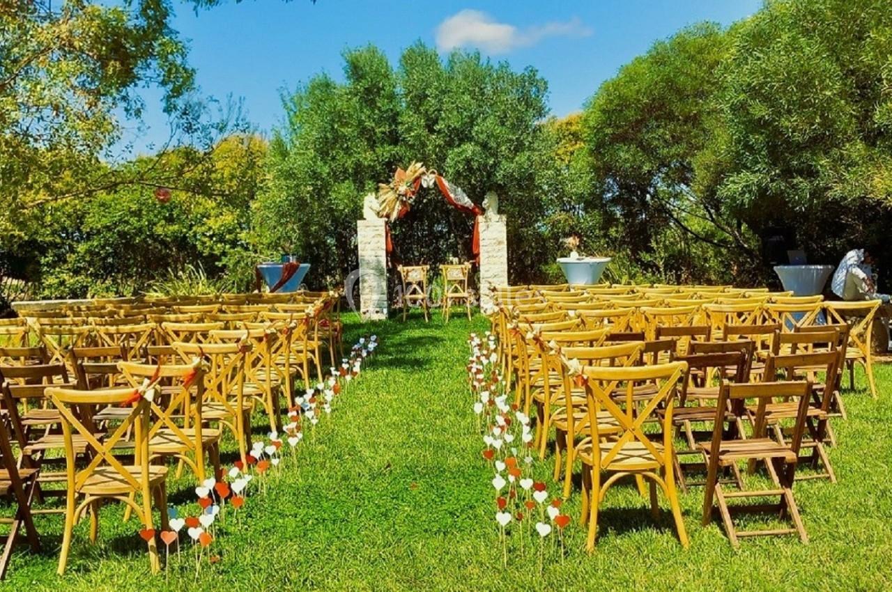 Chaises en bois disposées en rangées sur une pelouse, face à une arche décorée pour une cérémonie en extérieur.