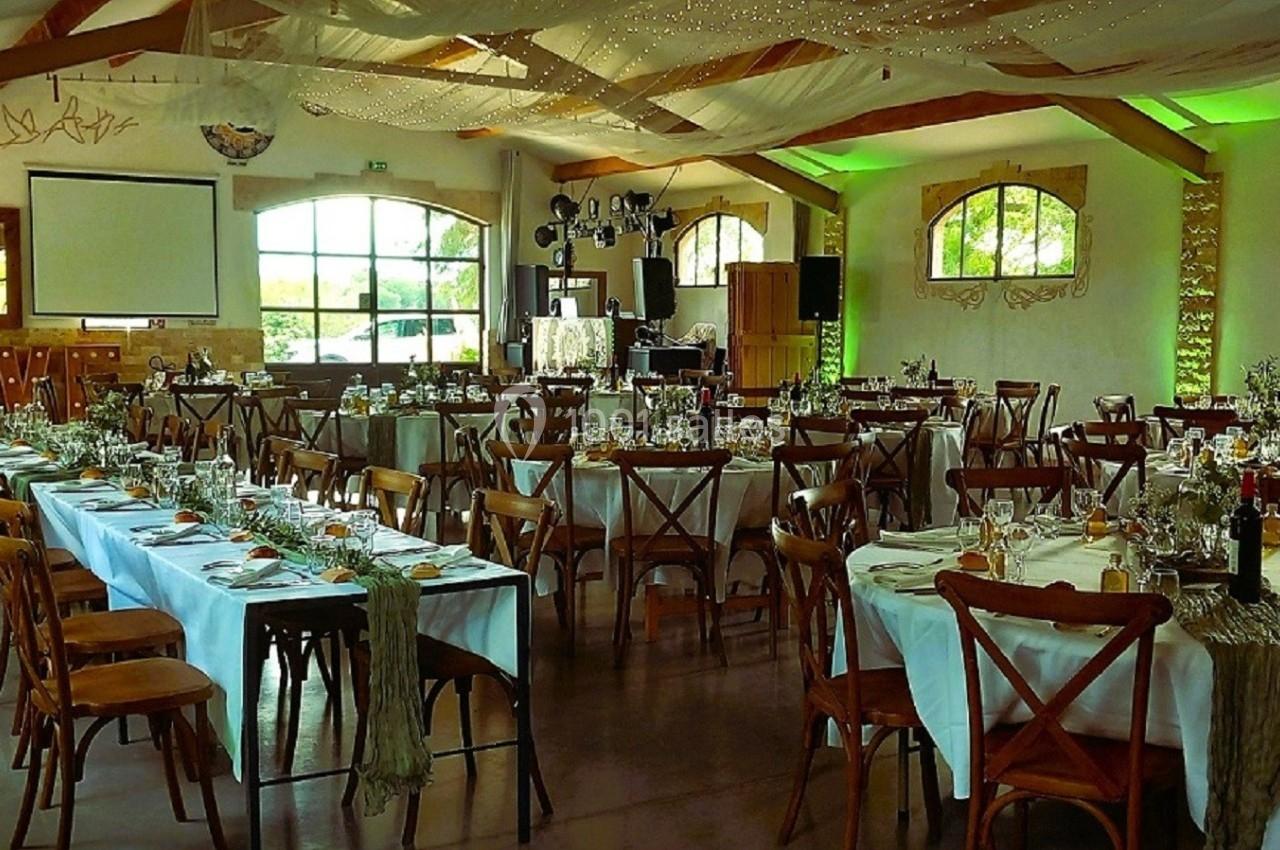 Salle de réception décorée pour un événement, avec tables dressées, nappes blanches et éclairage tamisé.