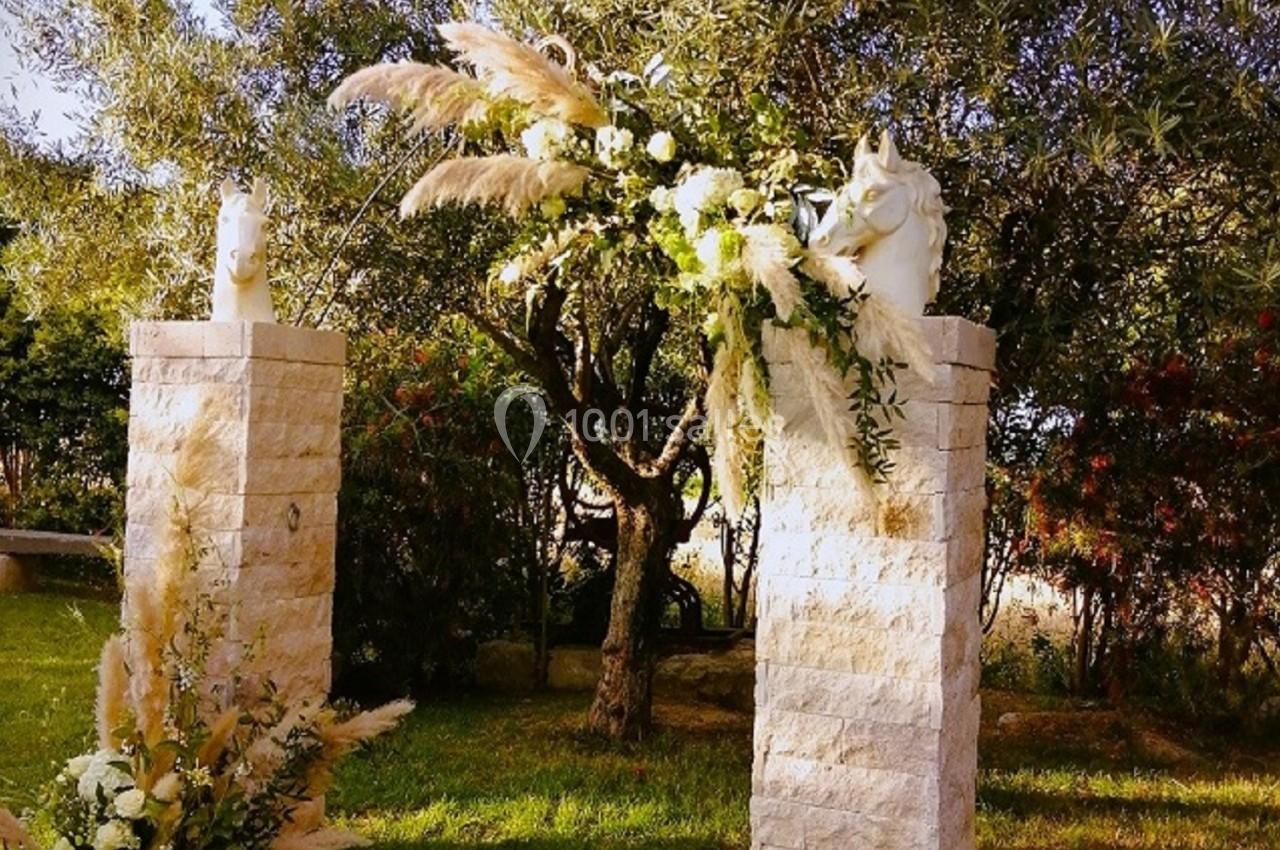 Deux colonnes en pierre décorées de fleurs et de feuillages, placées dans un jardin arboré.