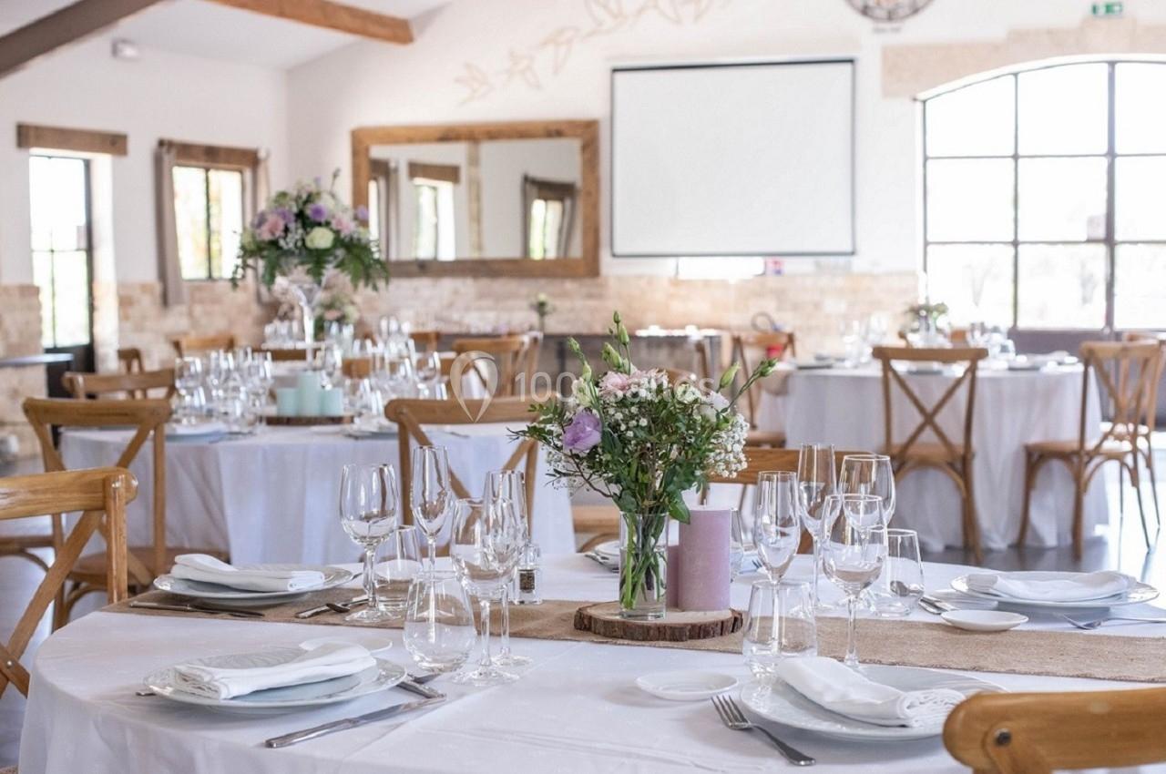 Salle de réception lumineuse avec tables décorées de fleurs, nappes blanches et vaisselle élégante.
