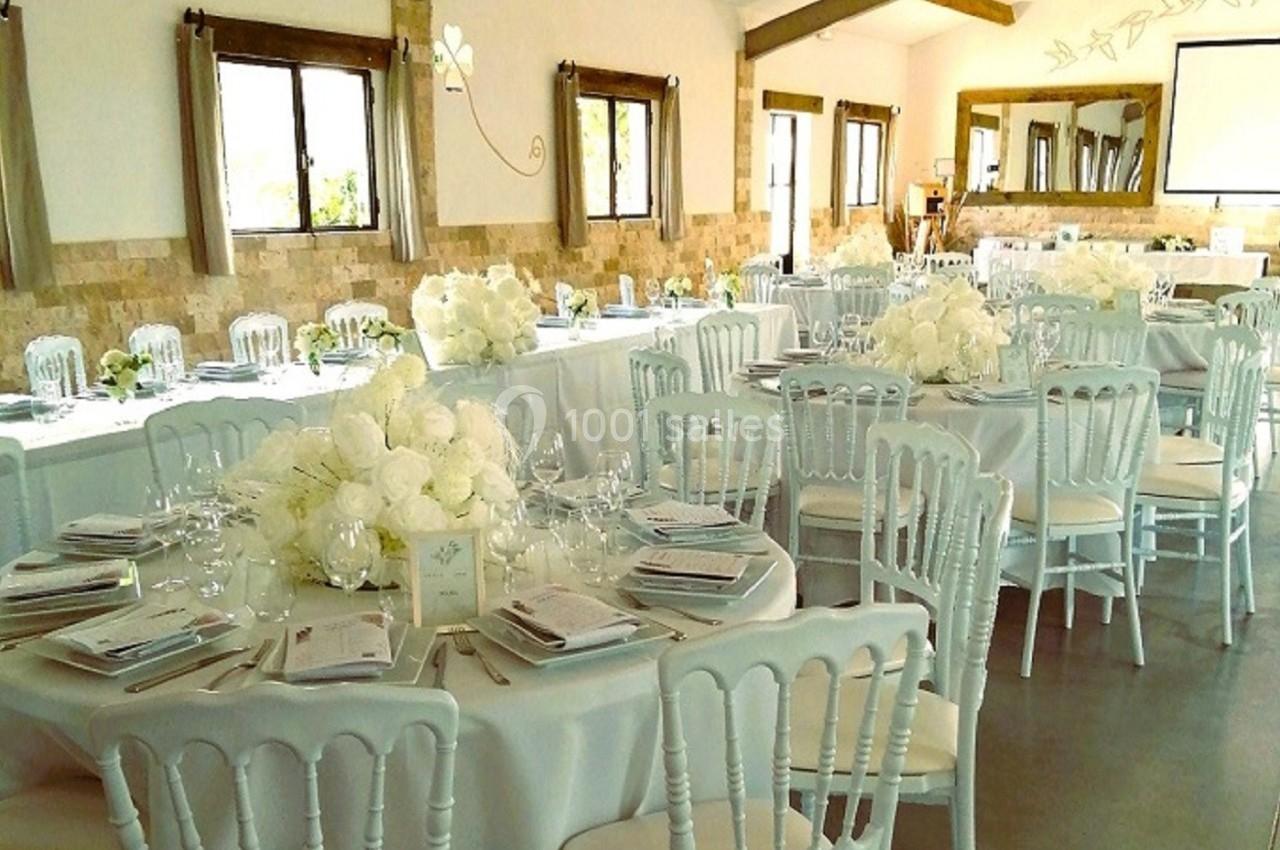 Salle de réception décorée avec des tables rondes, nappes blanches, chaises assorties et centres de table fleuris.