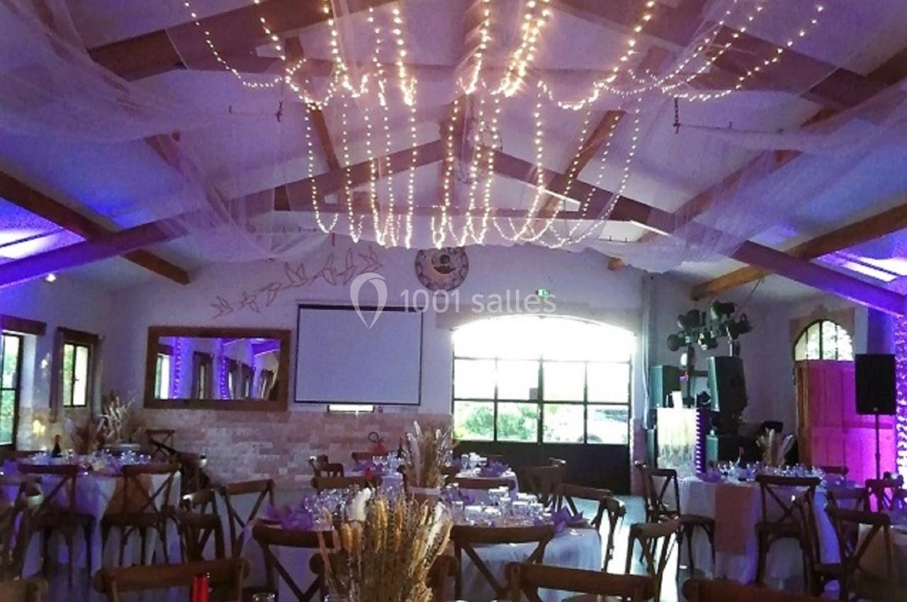 Salle de réception décorée avec des guirlandes lumineuses suspendues, tables dressées et ambiance chaleureuse.