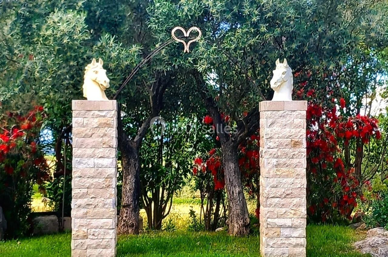 Deux colonnes en pierre surmontées de sculptures de têtes de chevaux, avec un cœur en métal suspendu entre elles.