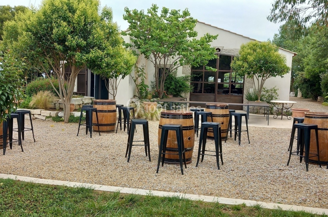 Terrasse extérieure avec tonneaux en bois servant de tables, entourée de tabourets noirs et de végétation.