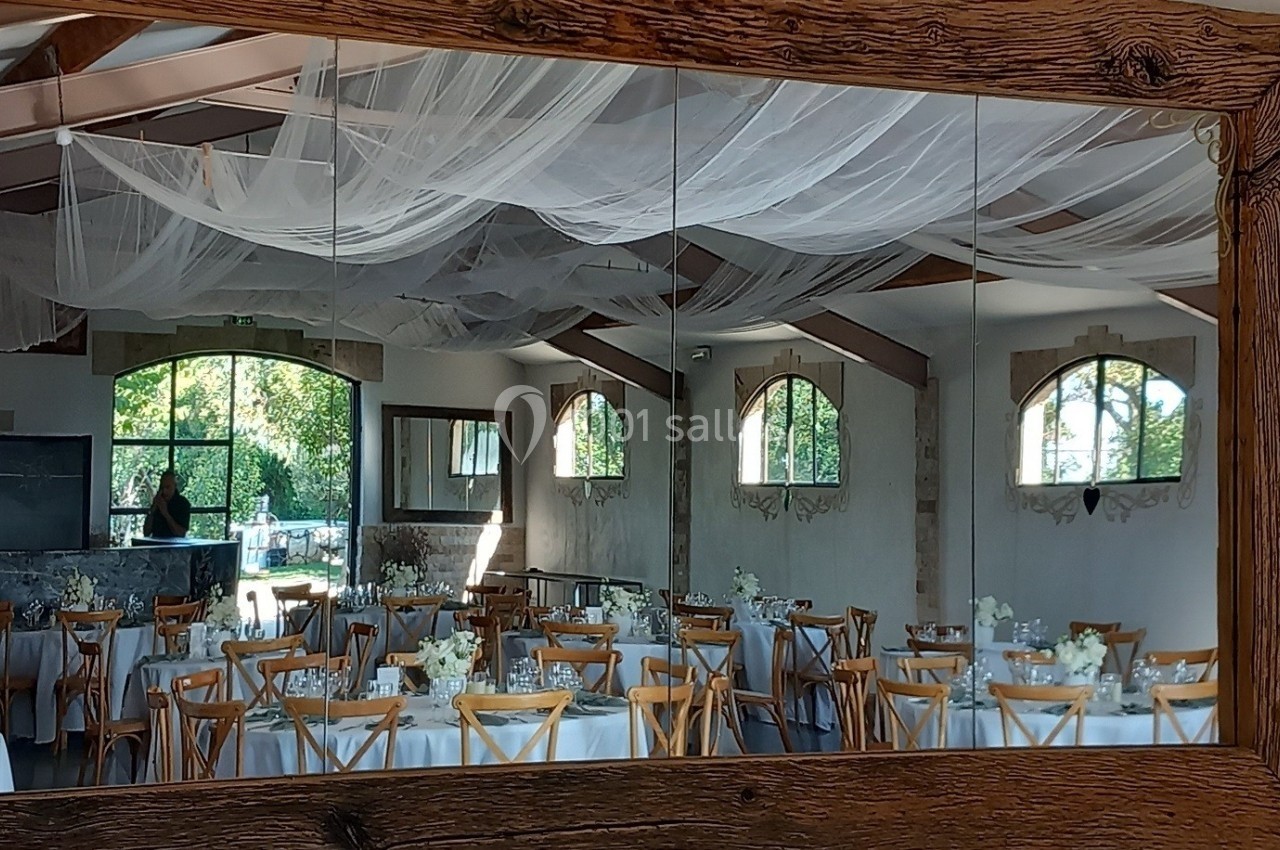 Reflet d'une salle de réception décorée avec des tables dressées et des chaises en bois, vue dans un miroir encadré de bois.