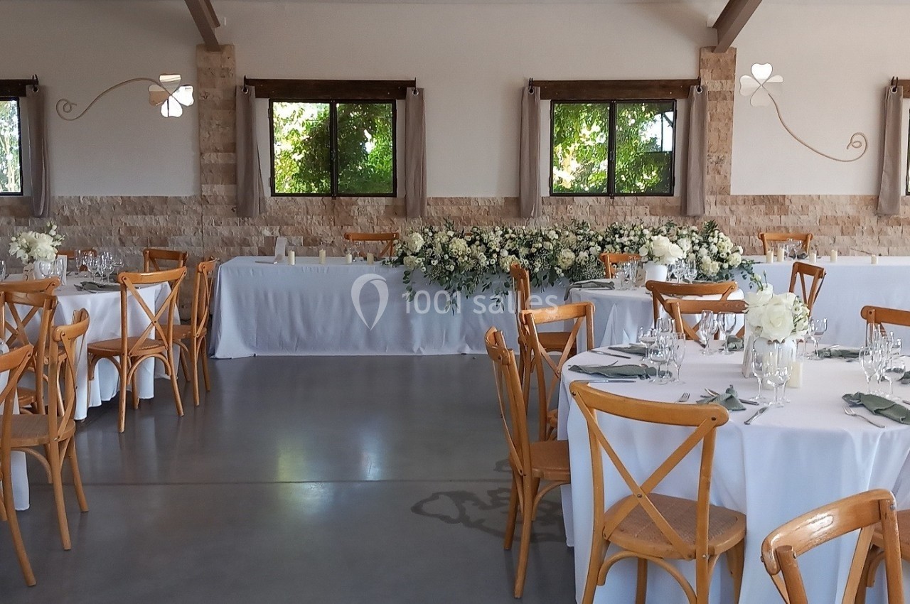 Salle de réception lumineuse avec tables rondes décorées de fleurs blanches et chaises en bois clair.