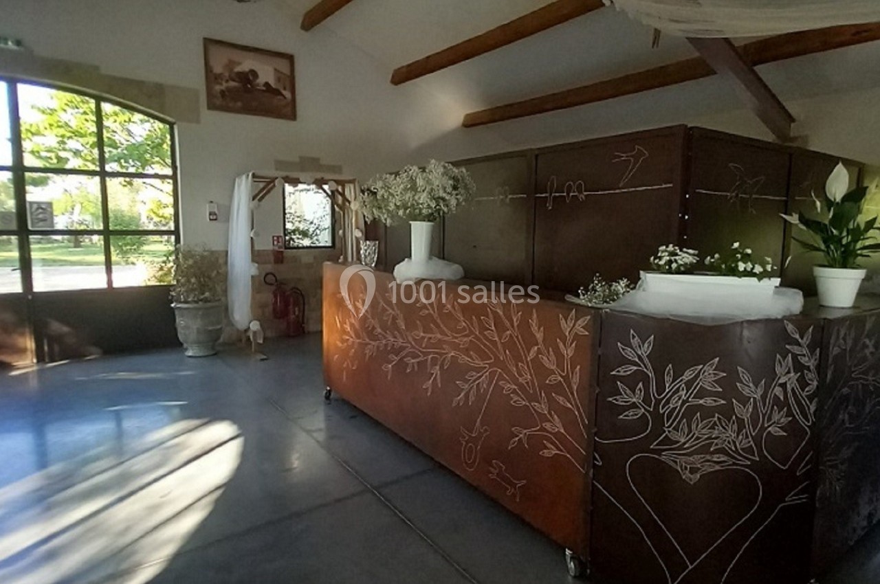 Comptoir en bois décoré de motifs gravés, situé dans une salle lumineuse avec de grandes fenêtres et des plantes.