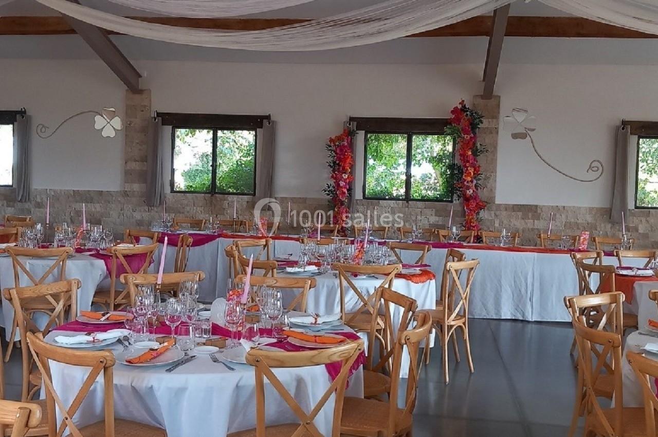Salle de réception décorée avec des tables rondes dressées, nappes blanches et accents colorés, sous un plafond drapé.
