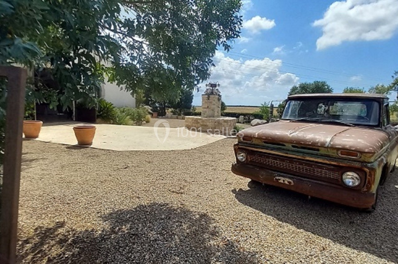 Camionnette ancienne rouillée stationnée sur une allée en gravier, entourée de végétation et d'un ciel dégagé.