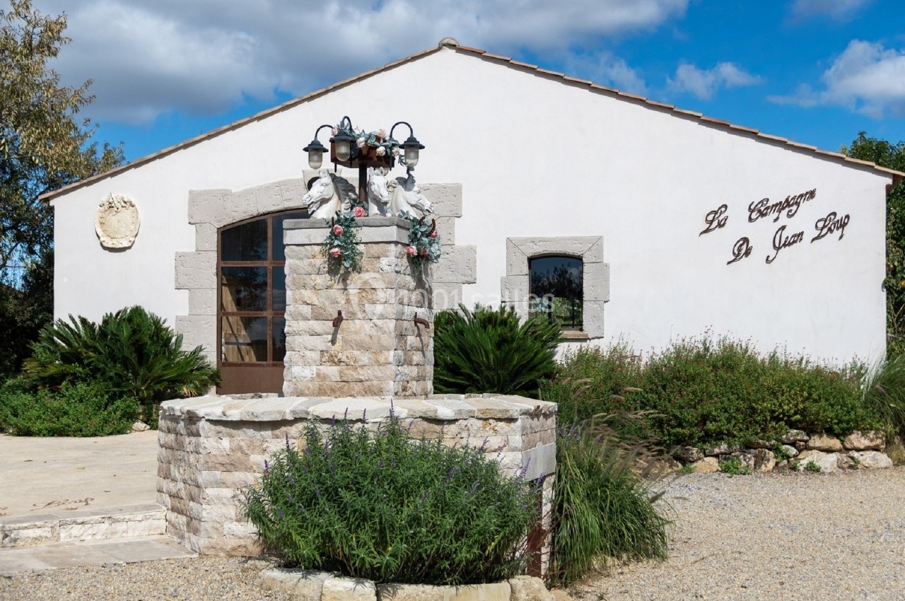 Façade d'un bâtiment blanc avec une fontaine en pierre ornée de fleurs au premier plan.