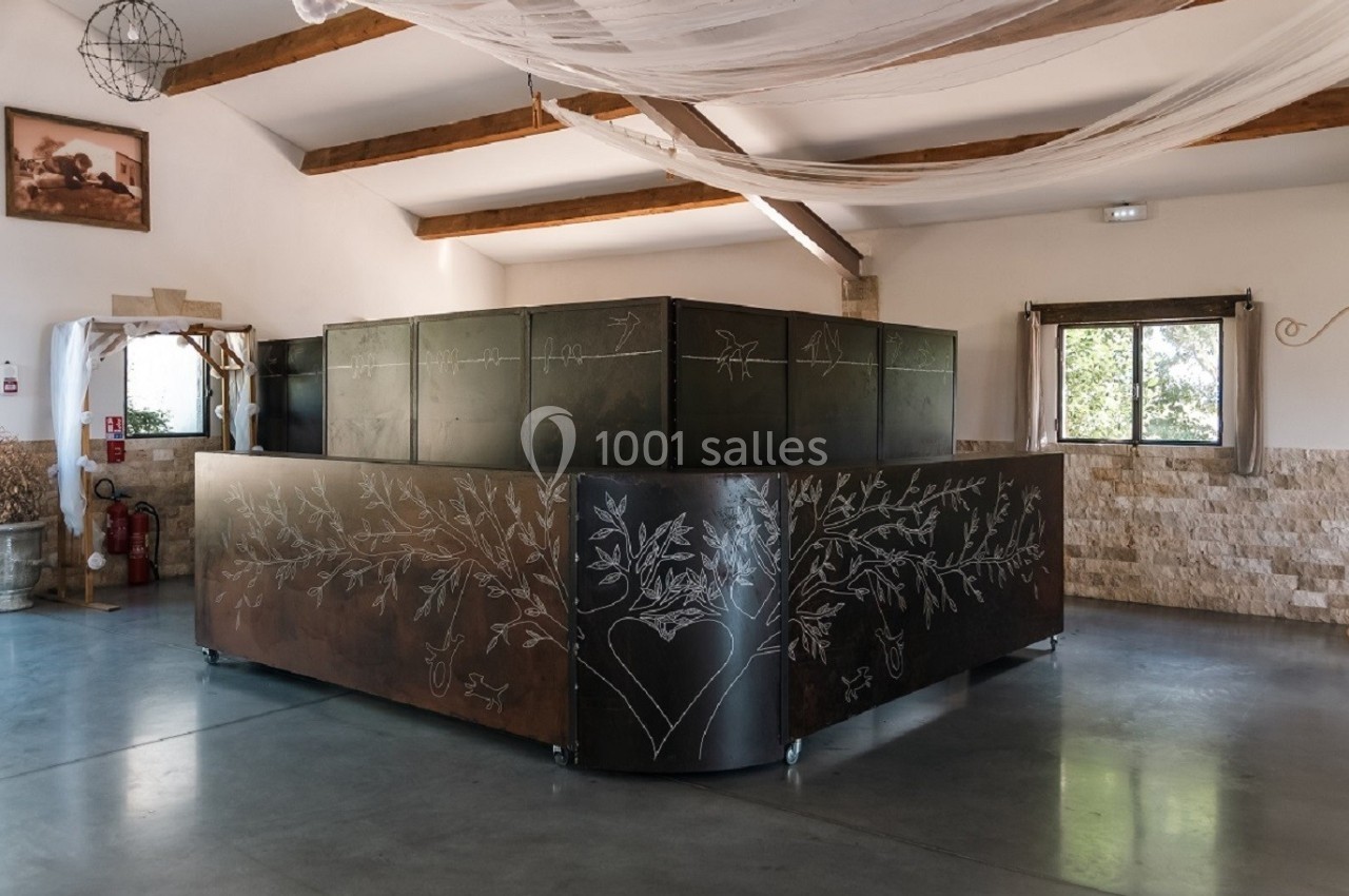 Comptoir en métal décoré de motifs gravés, installé dans une grande salle lumineuse avec poutres apparentes.