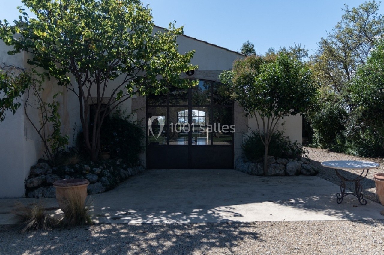 Façade d'un bâtiment avec une grande porte vitrée, entourée d'arbres et de végétation sous un ciel dégagé.