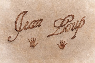 Texte ’Jean Loup’ écrit en calligraphie brune sur fond beige, accompagné de deux empreintes de mains.