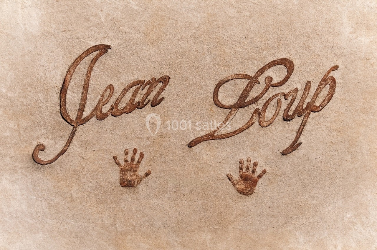 Texte ’Jean Loup’ écrit en calligraphie brune sur fond beige, accompagné de deux empreintes de mains.