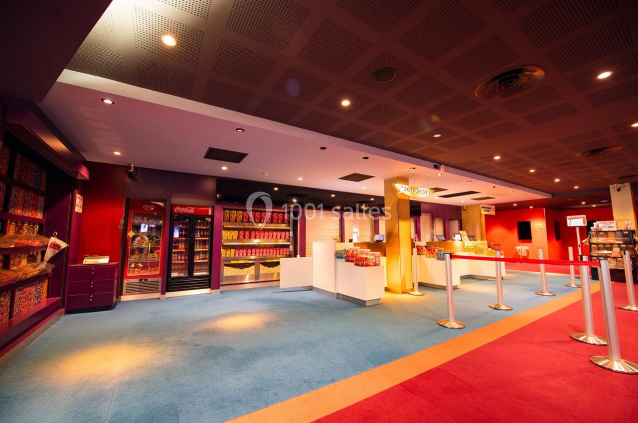 Vue d'un hall de cinéma avec un comptoir de confiseries, des distributeurs de boissons et un sol coloré.